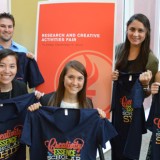 Group of people smiling and holding up T-shirts.
